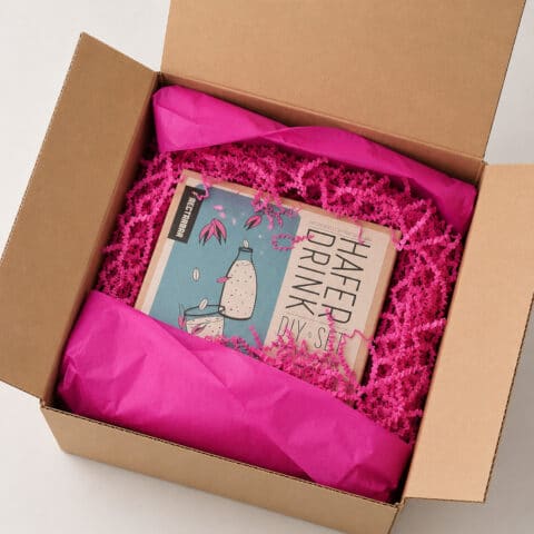 Geöffnete NECTARBAR Geschenkverpackung mit Haferdrink DIY-Set, pinkem Seidenpapier und Füllmaterial