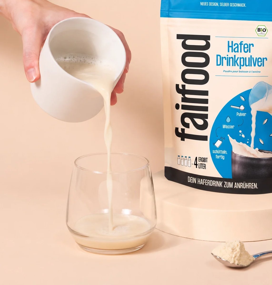 Angerührter Haferdrink wird aus einem Krug in ein Glas neben dem fairfood-Beutel gegossen