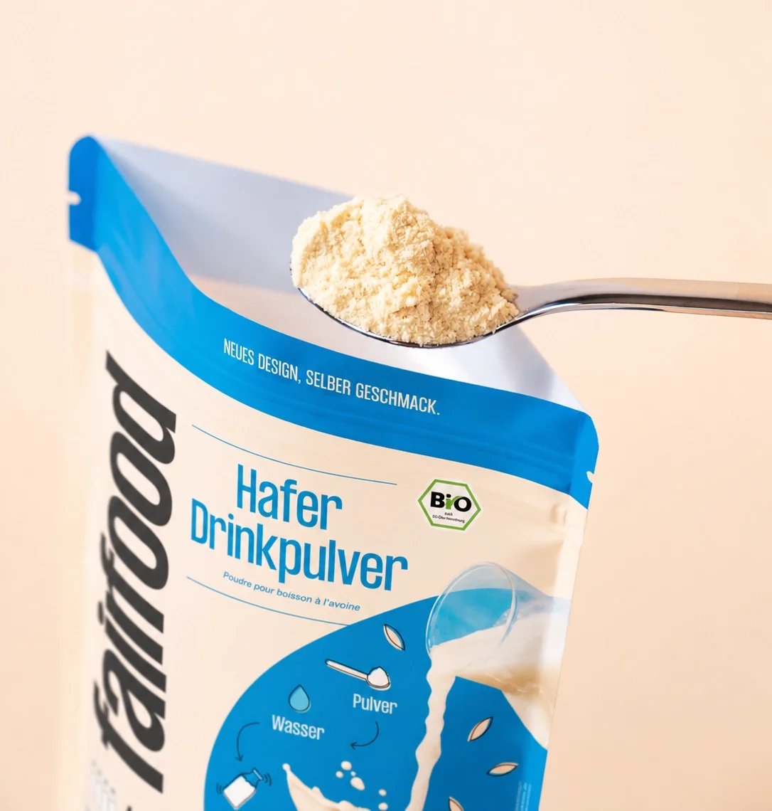 Gehäufter Löffel Haferdrinkpulver über dem geöffneten fairfood-Beutel